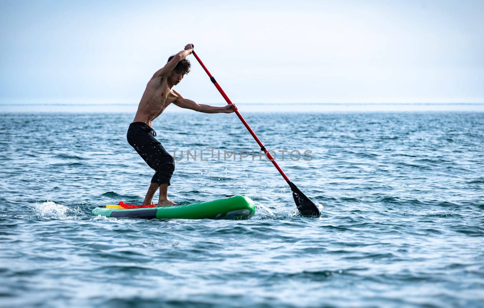 a sporty guy swims on a sup board with a paddle on the sea during the day against a beautiful sky in summer