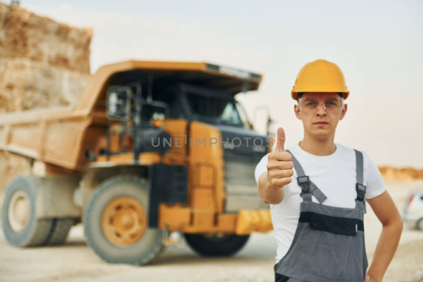 In glasses and hard hat. Worker in professional uniform is on the borrow pit at daytime.