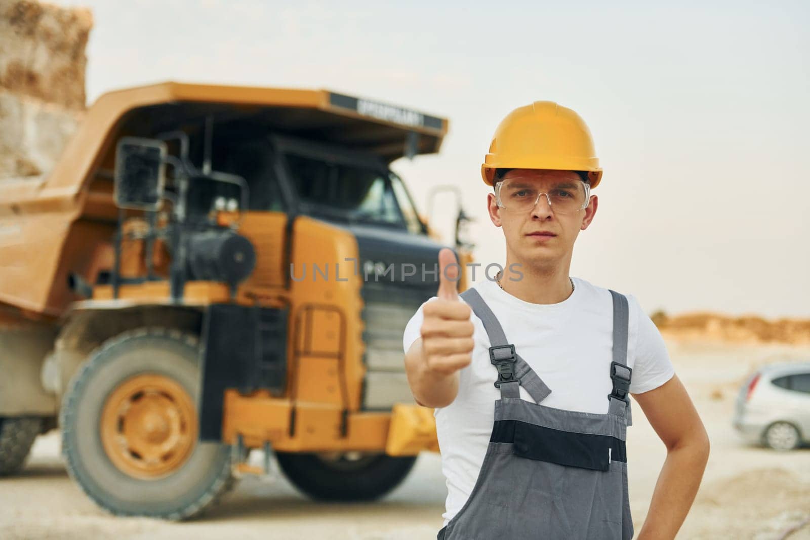 In glasses and hard hat. Worker in professional uniform is on the borrow pit at daytime.