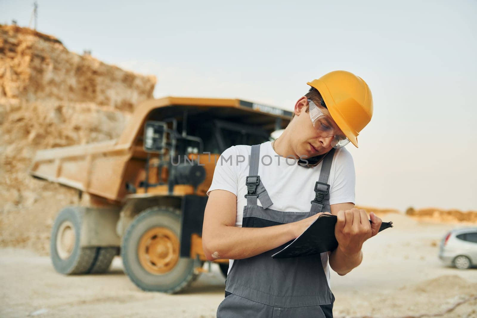 Manager planning the work. Man in professional uniform is on the borrow pit at daytime.