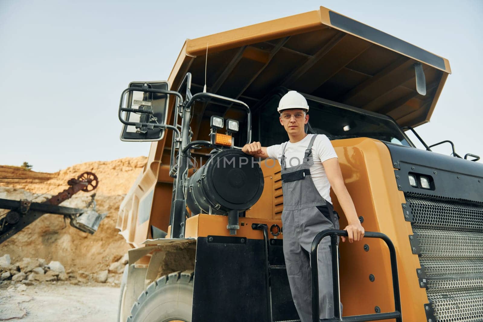 On the vehicle. Worker in professional uniform is on the borrow pit at daytime.