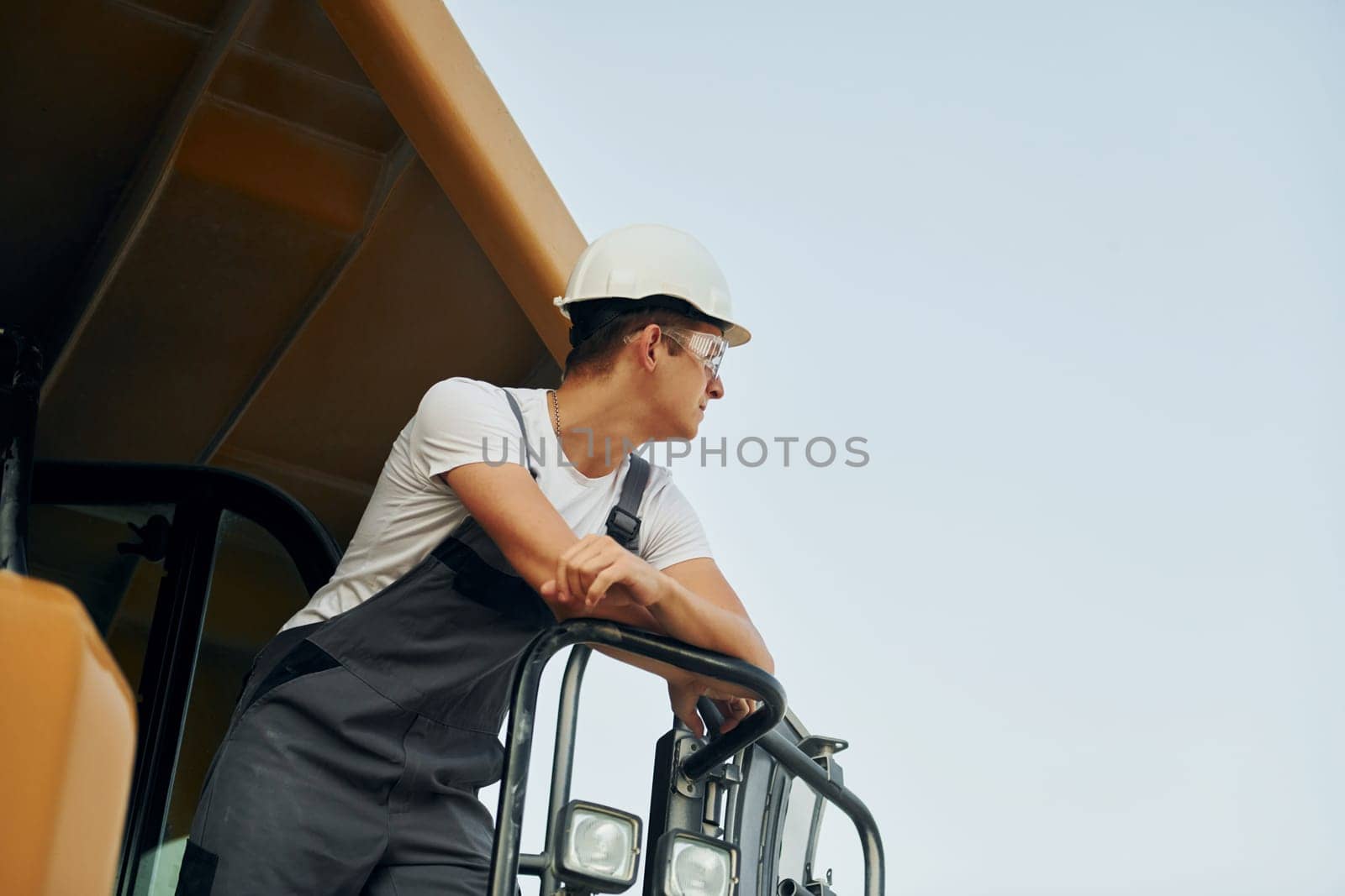 On the vehicle. Worker in professional uniform is on the borrow pit at daytime.