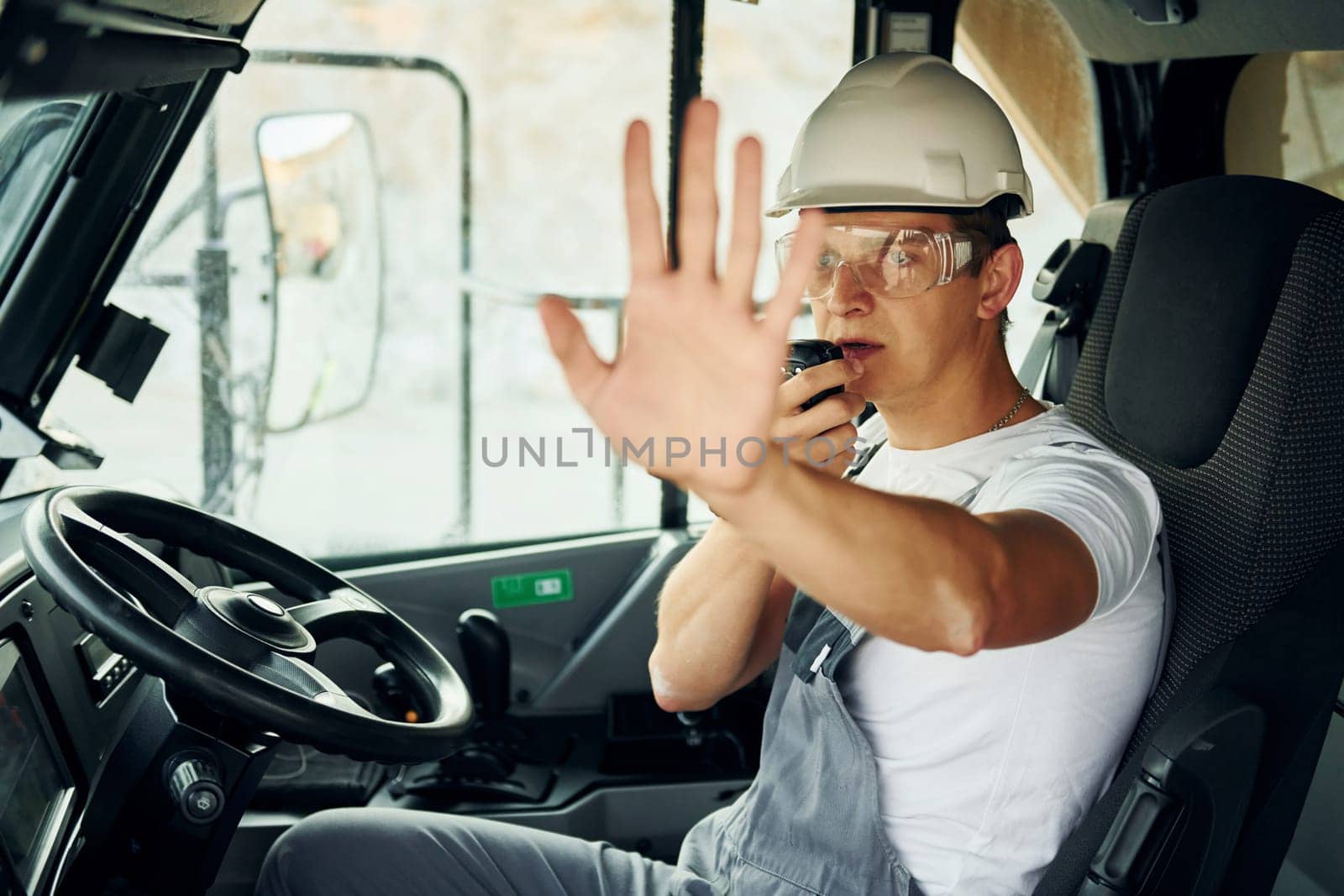 Driver is at work. Man in professional uniform is on the borrow pit at daytime.