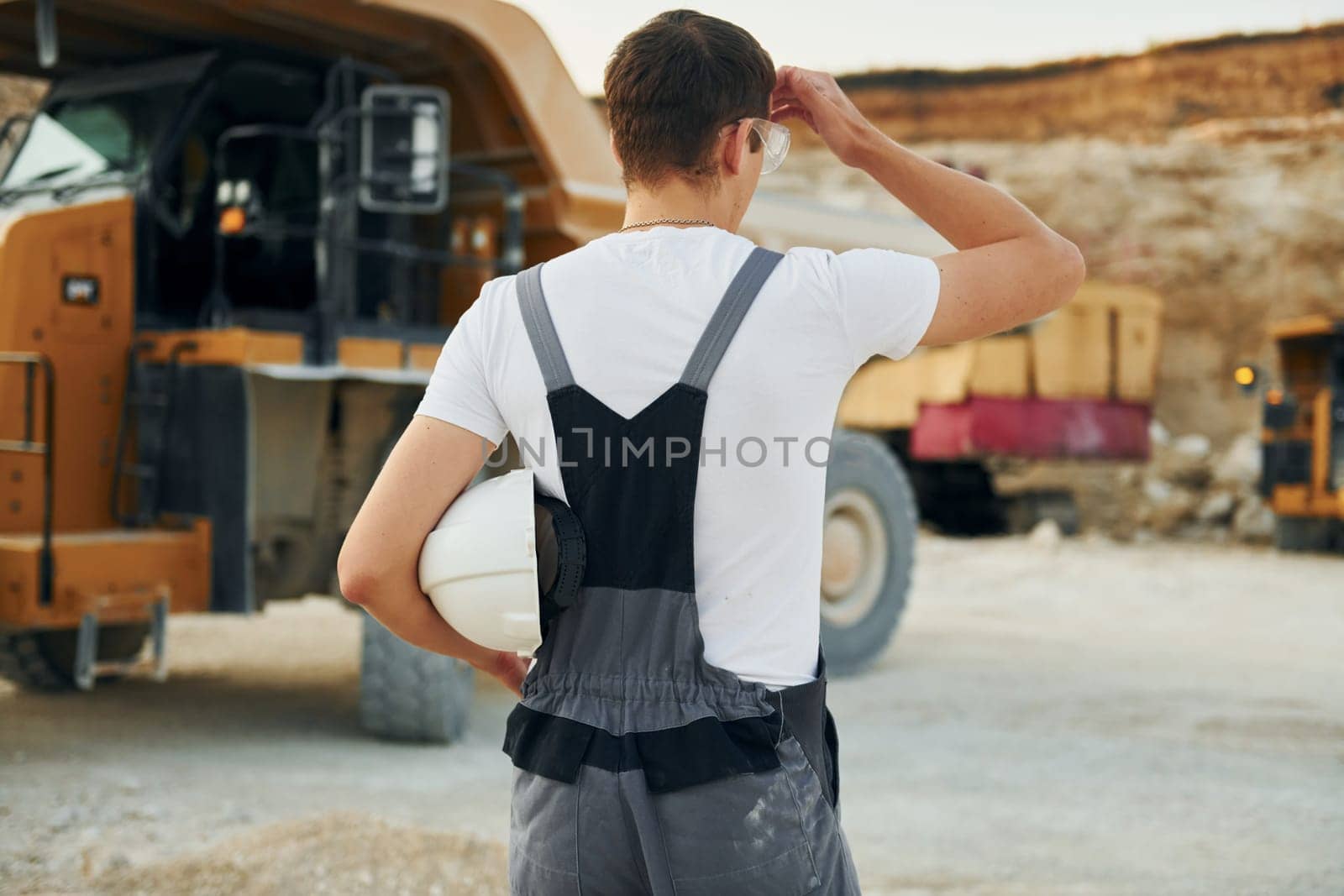Rear view. Worker in professional uniform is on the borrow pit at daytime.