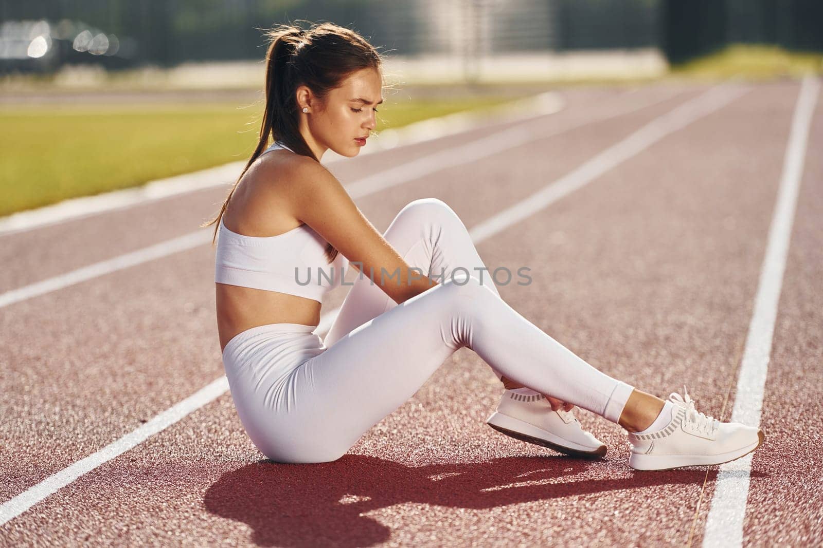 On the ground. Young woman in sportive clothes is exercising outdoors.