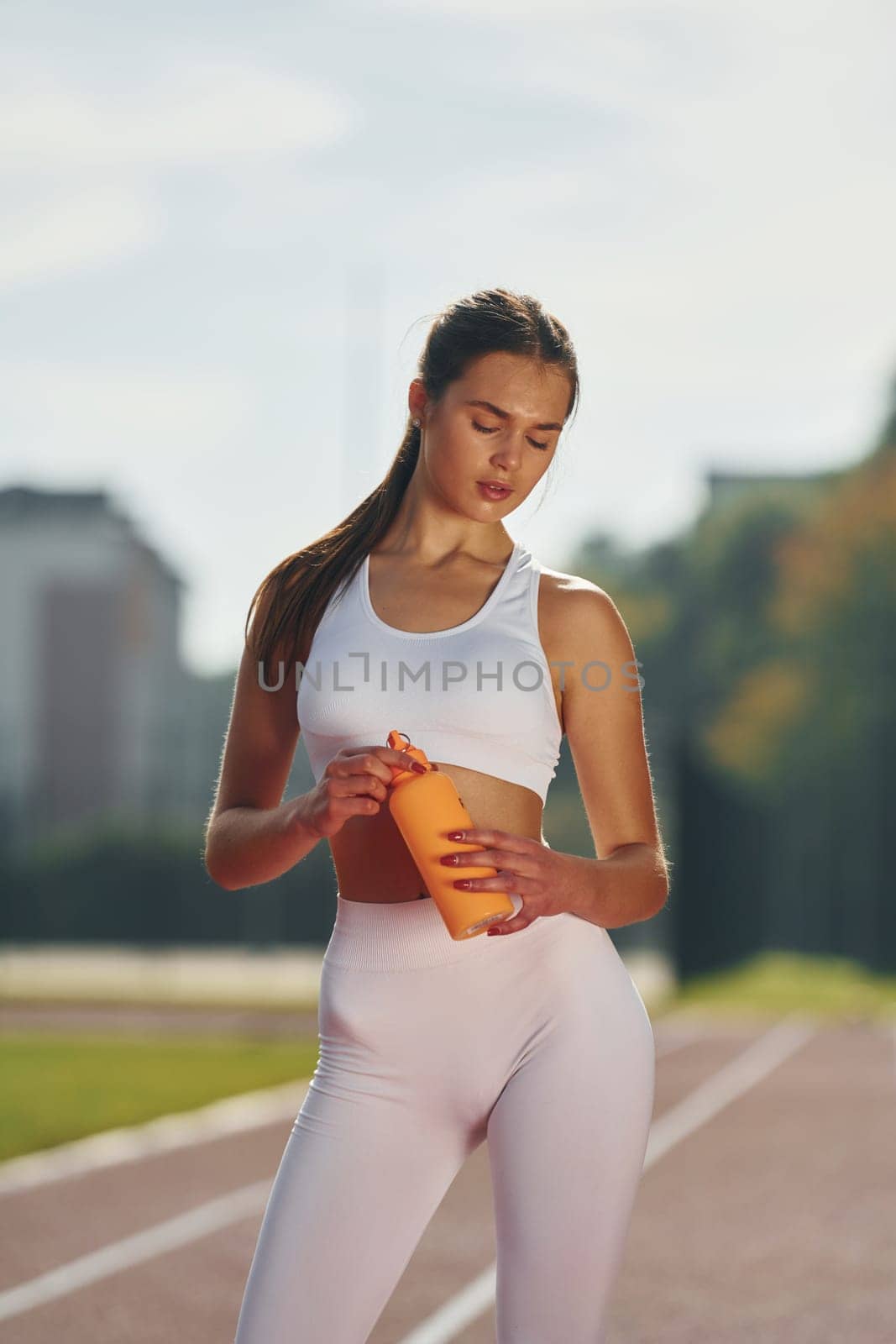 Holding bottle of watter. Young woman in sportive clothes is exercising outdoors.