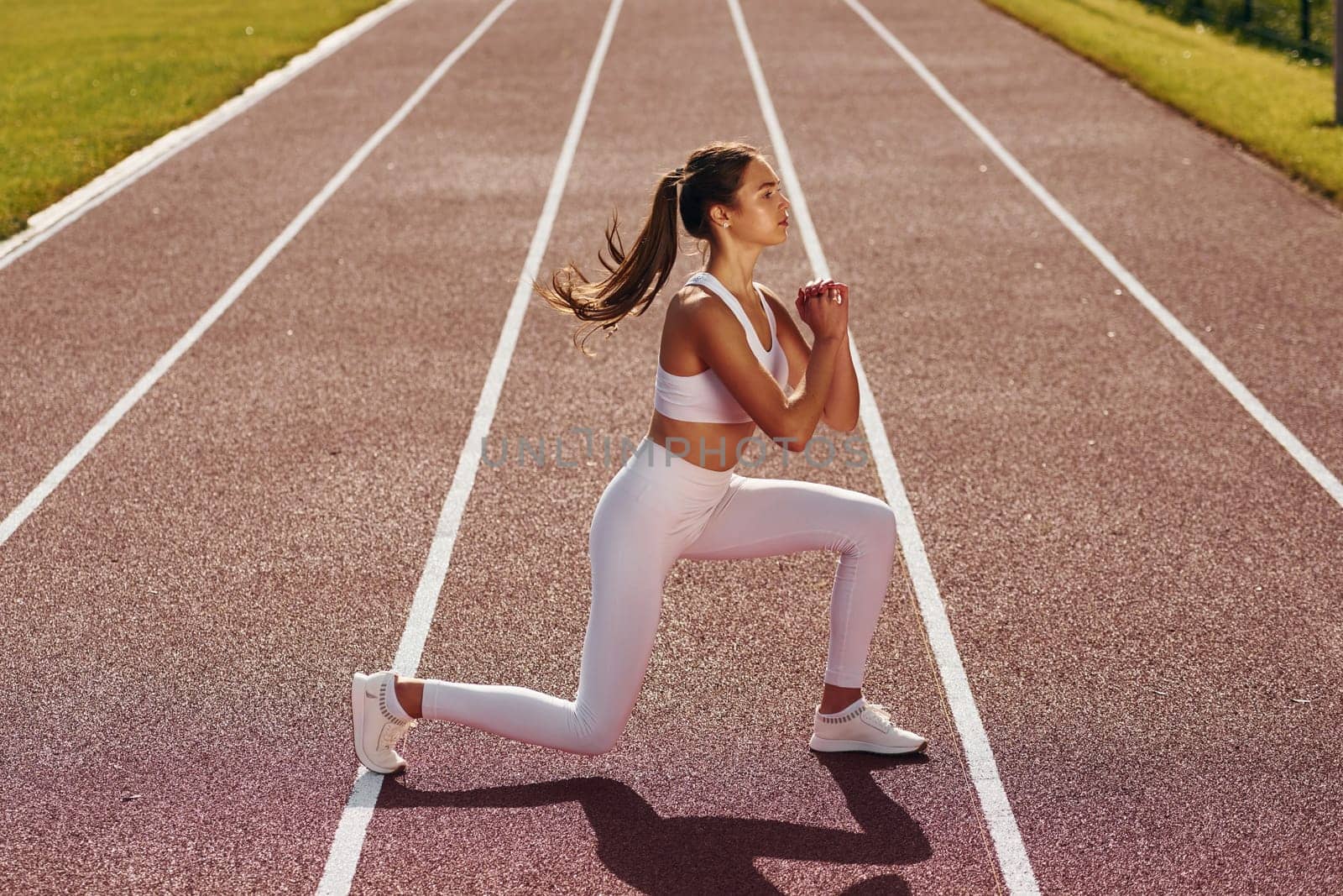 Doing squats. Young woman in sportive clothes is exercising outdoors.
