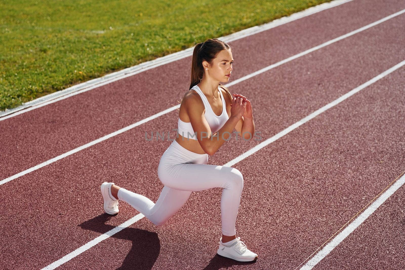 Doing squats. Young woman in sportive clothes is exercising outdoors.