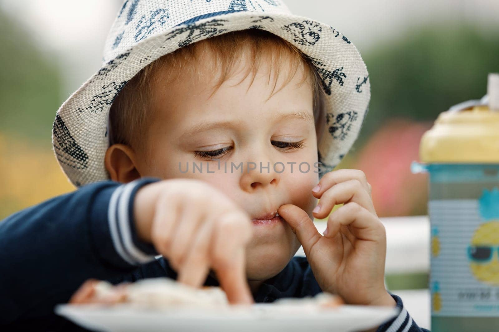 The boy in the summer garden chooses and tastes food from a plate.