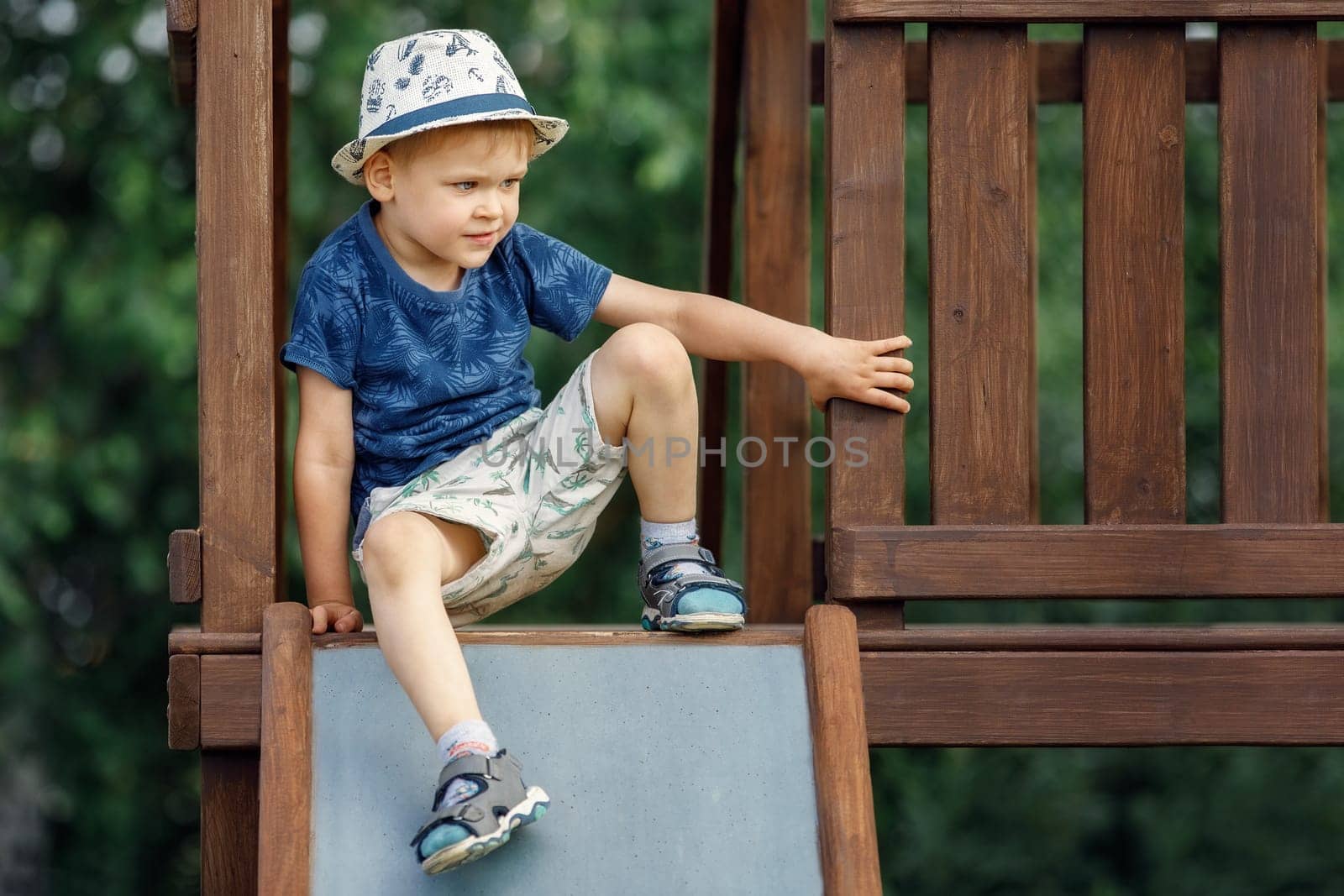 A child climbs up on the wooden playground and prepares to slide on a metal slide.