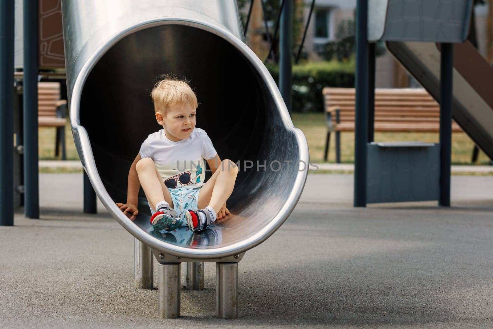 Cute boy sitting relaxed in the tube on playground.