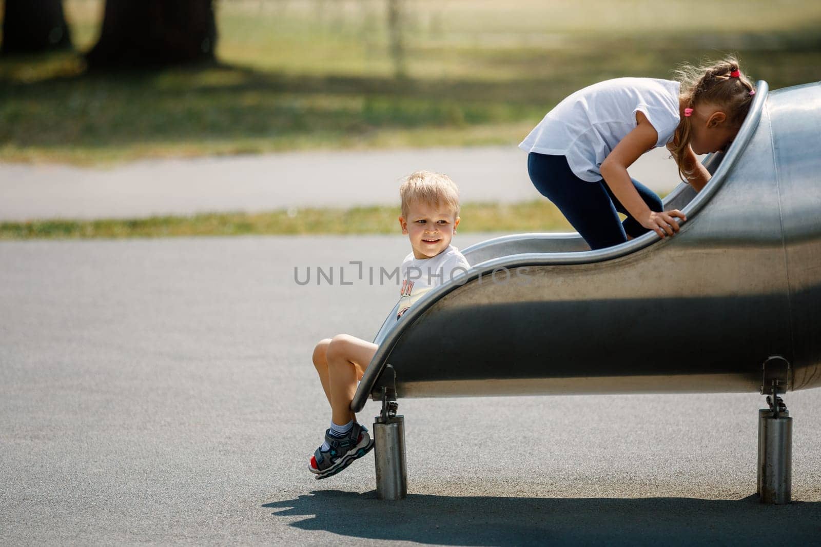 Cute boy sitting relaxed in the tube on playground, and the girl goes back to the tunnel by Lincikas