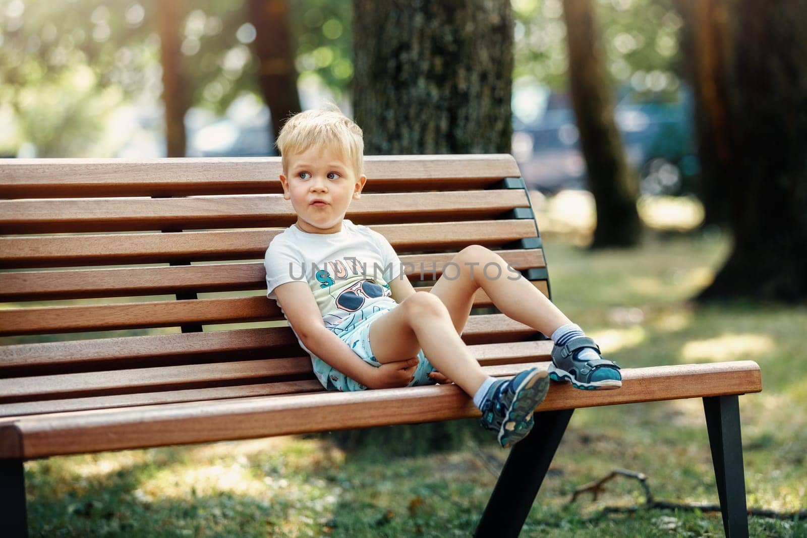 Cute kid boy sitting on a bench in the park and rest.