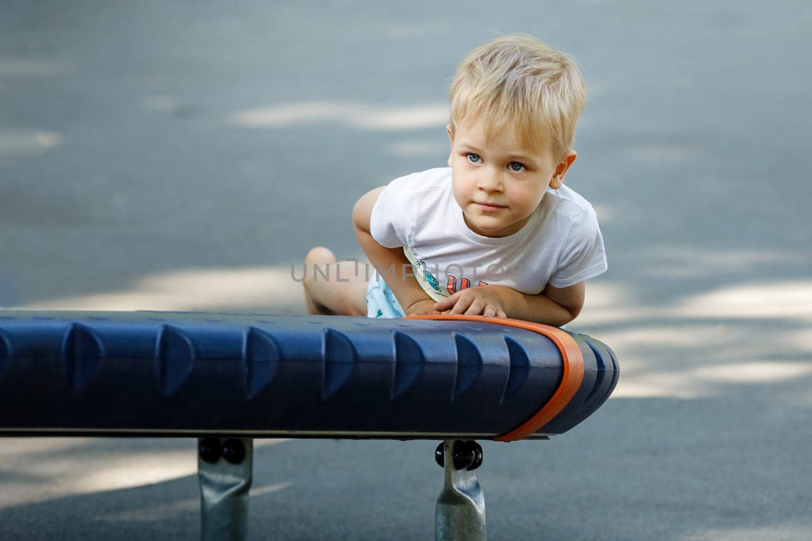 Portrait of a little boy in an outdoor sports gym, a child lies on the gymnastic exercises equipment by Lincikas