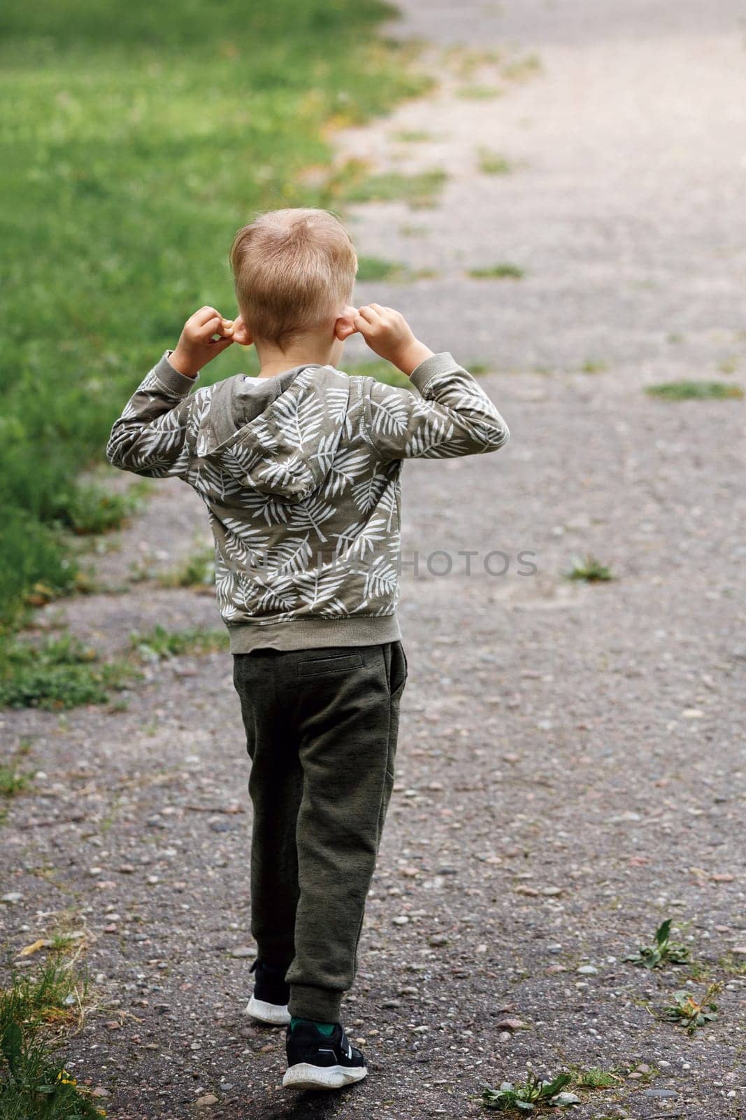 The little boy walks down the road, (rear view) he stretches his ears hard, the child experiments with his body.