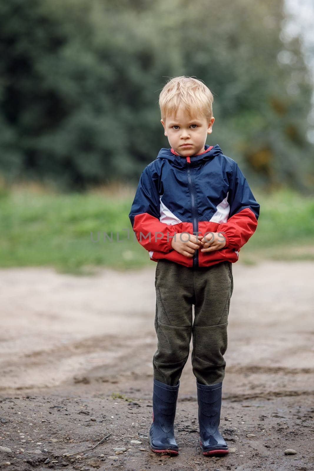 Portrait of a sad lonely boy in bad weather in autumn. The end of summer fun. Dirt and humidity outdoors there is no activity for children.