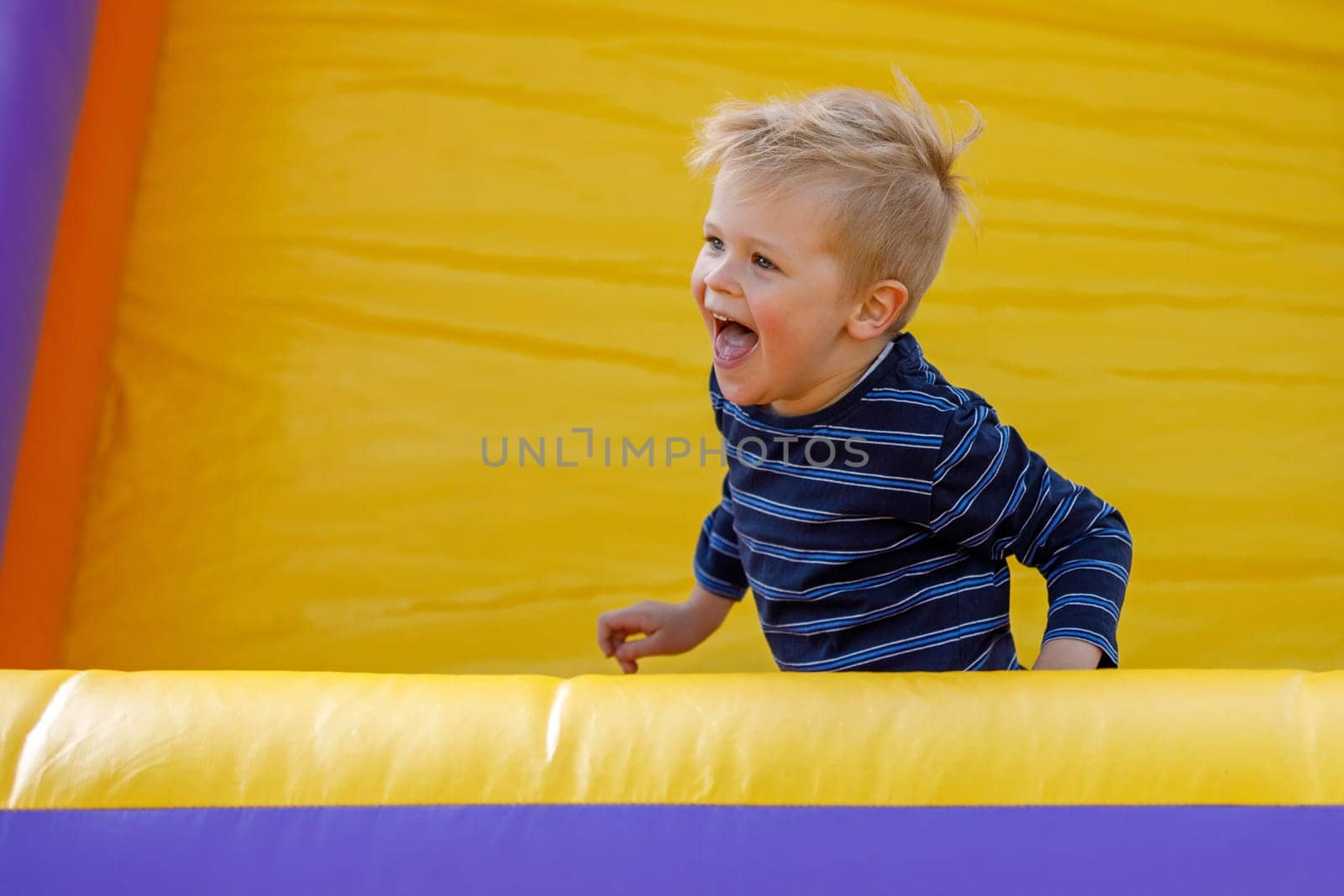 Stormy child be naughty on playground trampoline. Little cool boy have fun on a yellow inflatable trampoline. by Lincikas