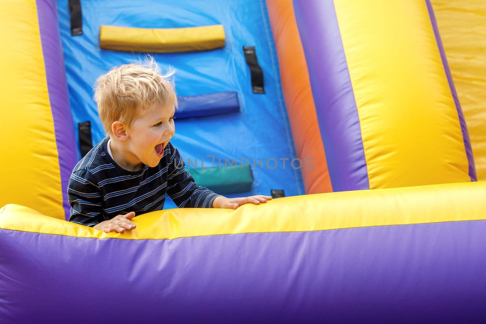 Joyful child jumping on colorful inflatable trampoline. Little boy 3-4 years playing on outdoors playground in sunny summer day. Kids fun activity concept. Children's leisure.