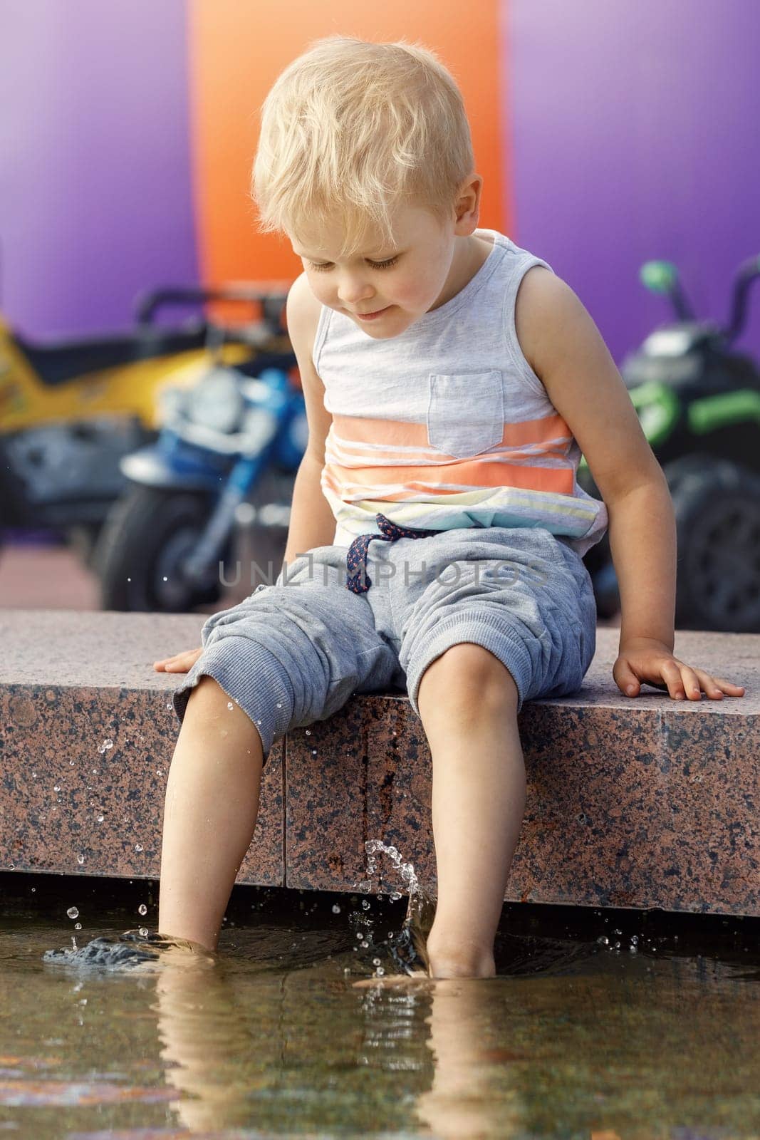 Little barefoot boy plays with water near the fountain in a big city during the summer heat. They escape from the summer heat.