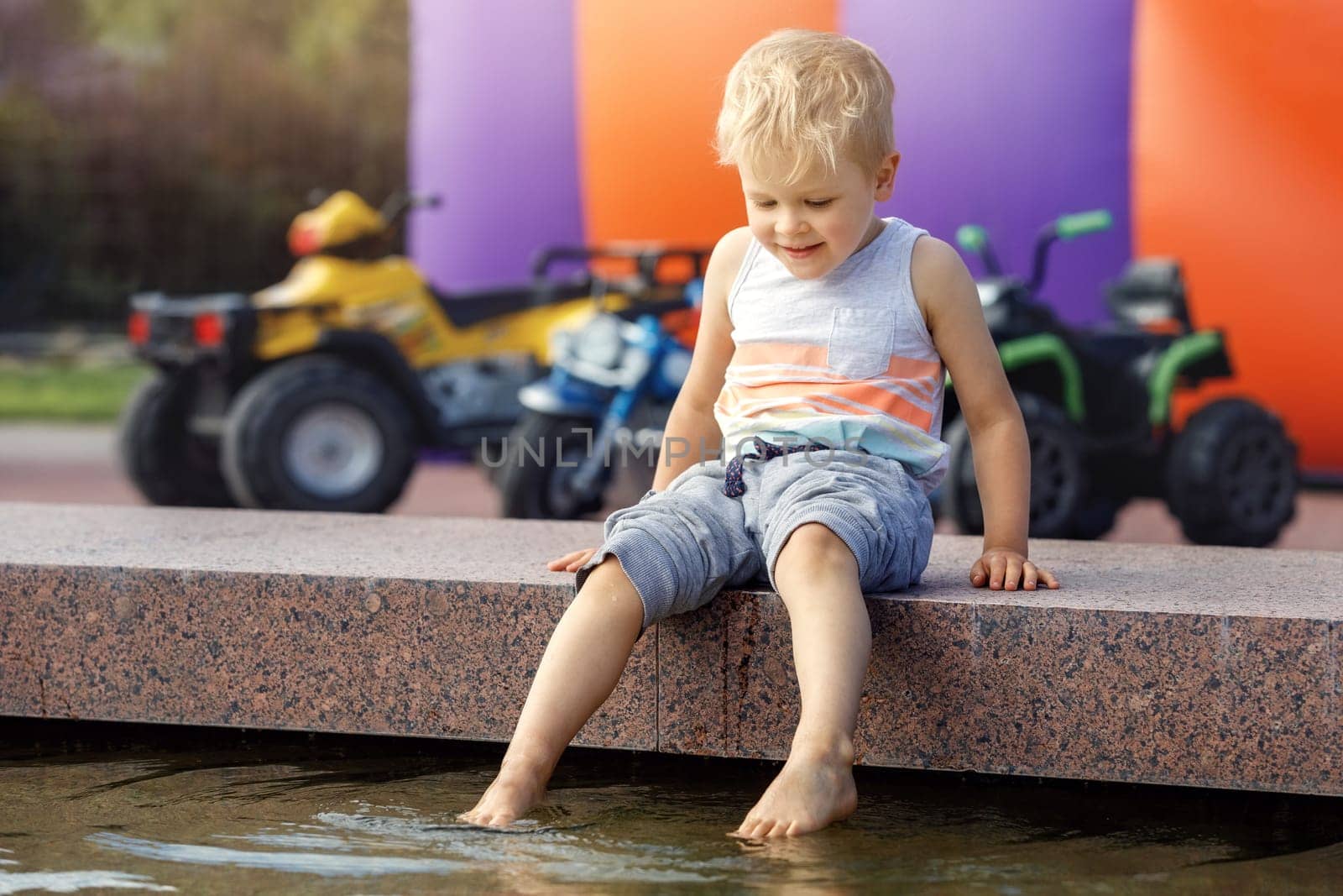 Little boy plays and cools feet in fountain water on a hot summer day.