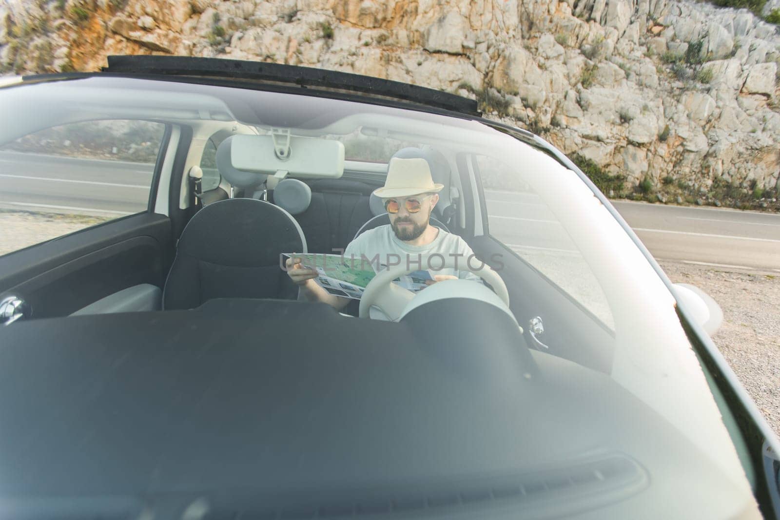 Hipster man looking on location navigation map in car, tourist traveler driving and hold in male hands europe cartography, view and plan tourist way road, trip in transportation cabriolet auto by Satura86
