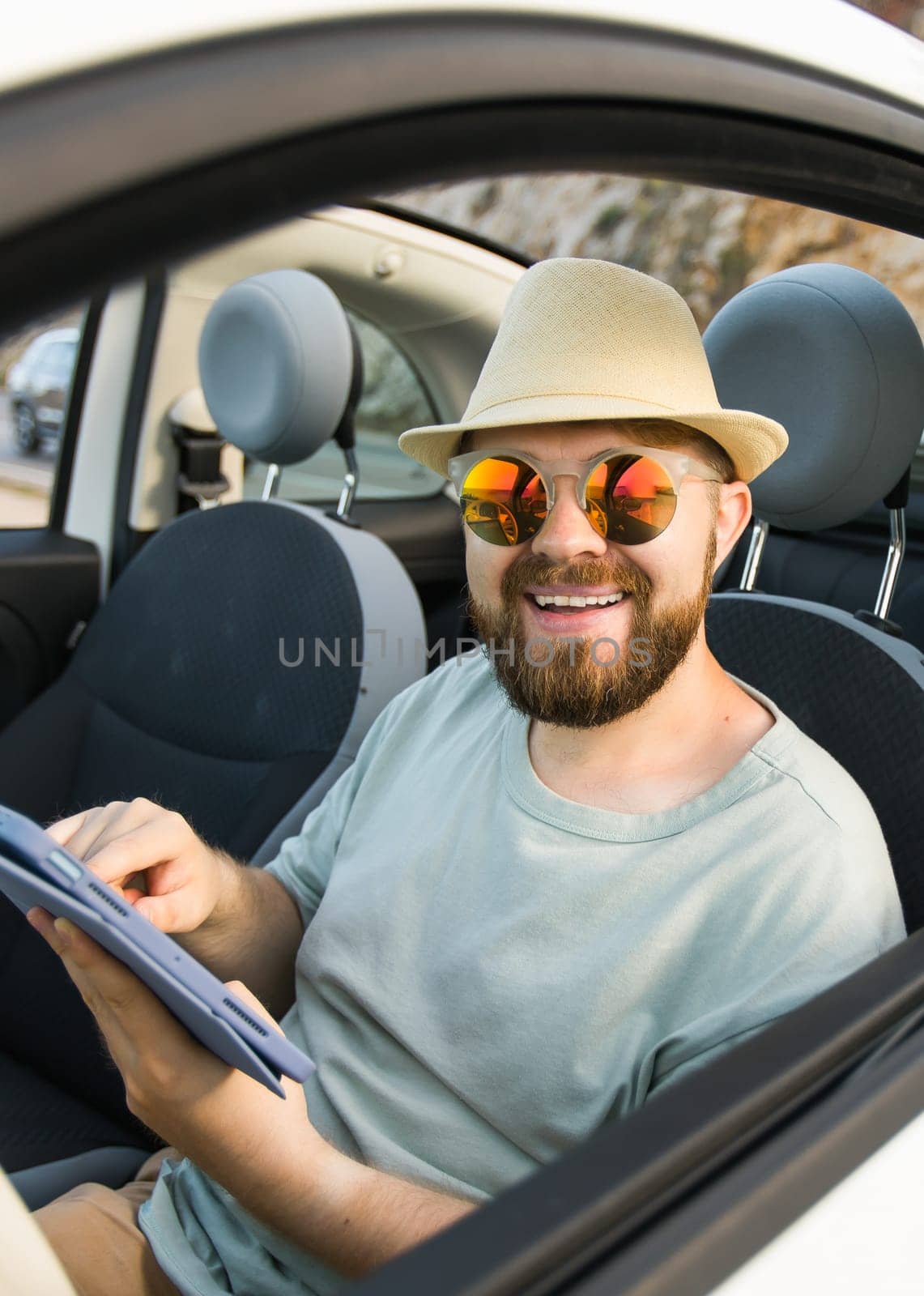 Bearded man using digital tablet inside car while travel and road trip vacation holidays - road map and navigation