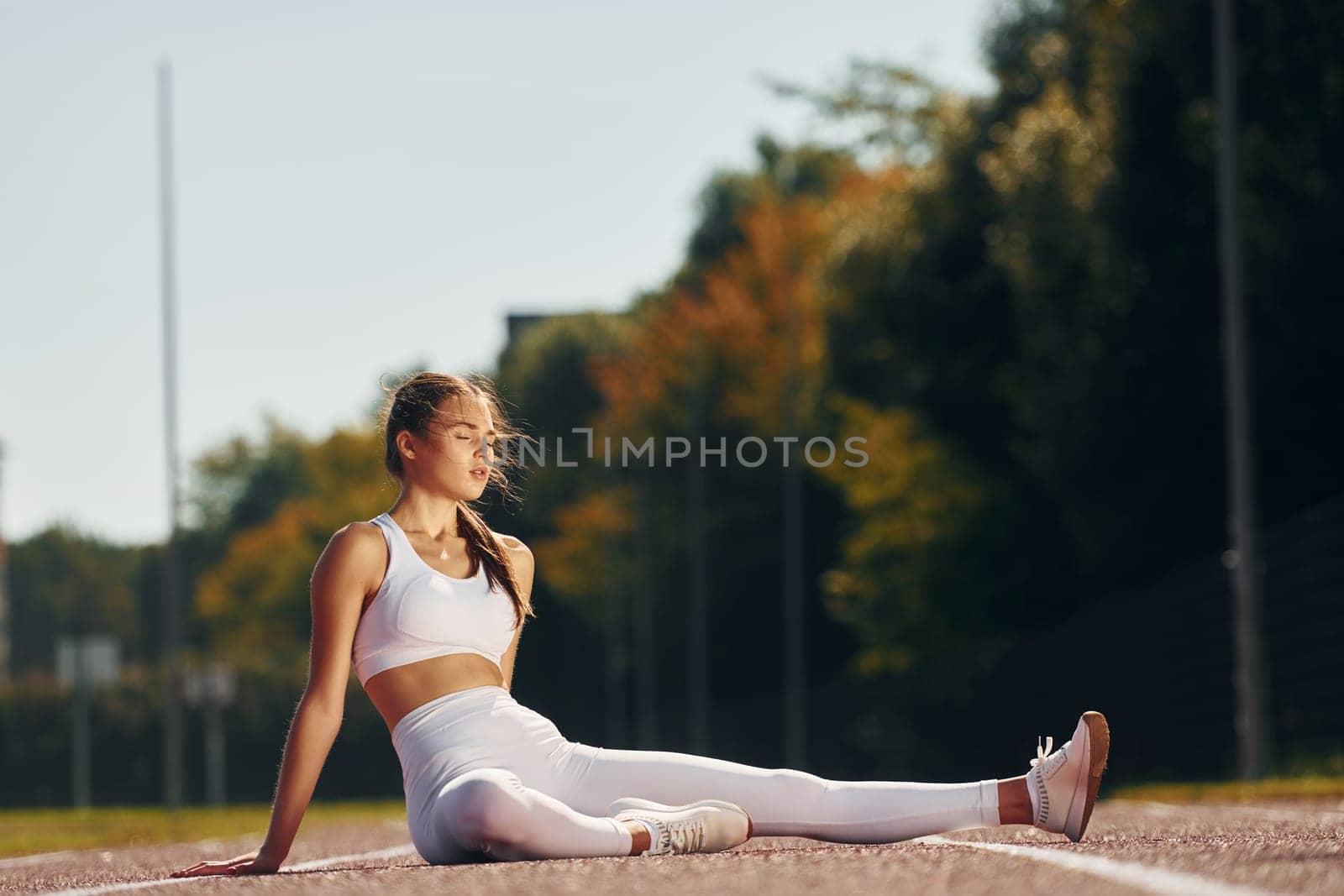 Sitting on the ground. Young woman in sportive clothes is exercising outdoors.