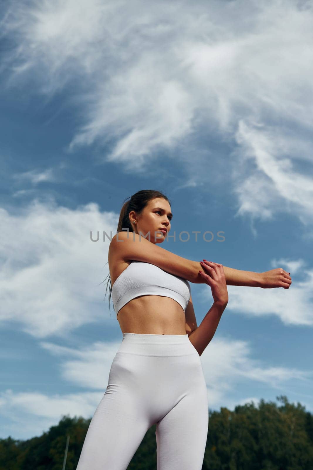 Cloudy sky. Young woman in sportive clothes is exercising outdoors.
