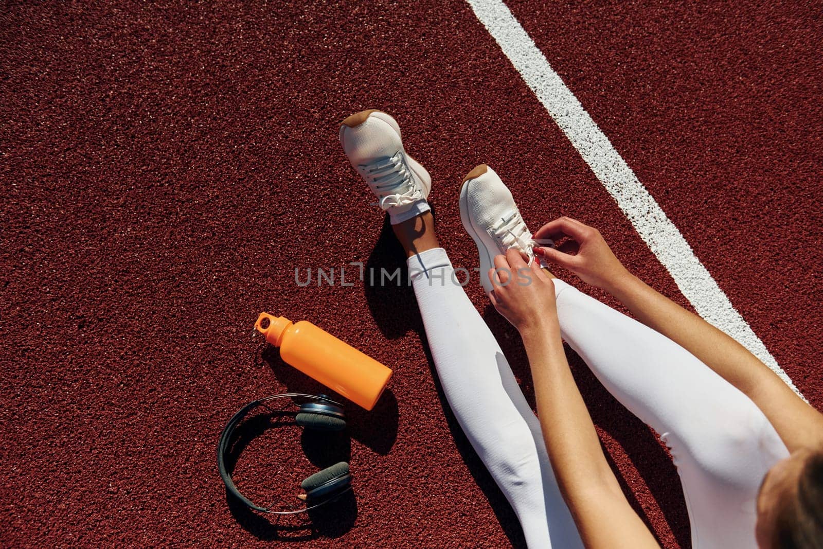 Top view of woman's legs, bottle of water and headphones.