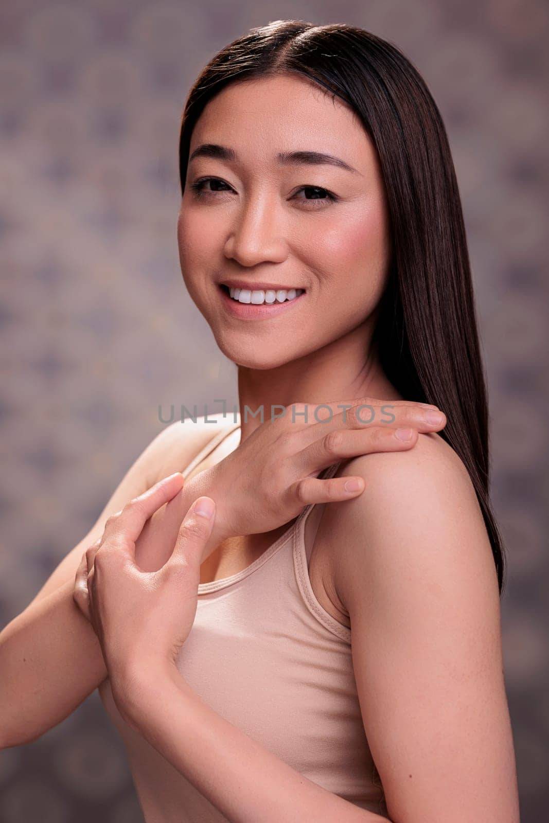 Young smiling asian woman touching shoulder and showing body care concept. Attractive woman demonstrating femininity, tenderness and natural beauty, posing for studio portrait