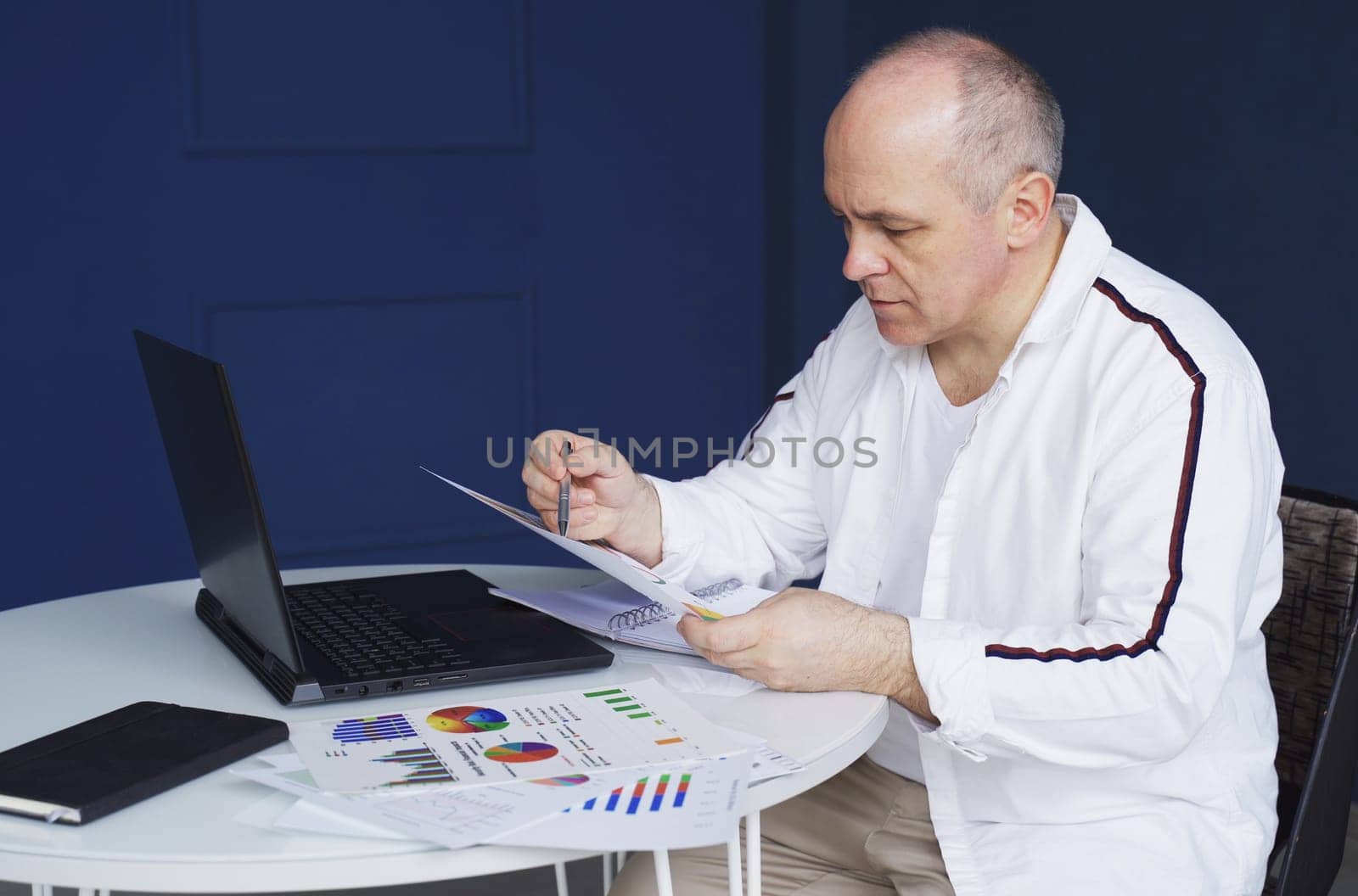 Male businessman works on laptop, studies reporting documents, charts and graphs.