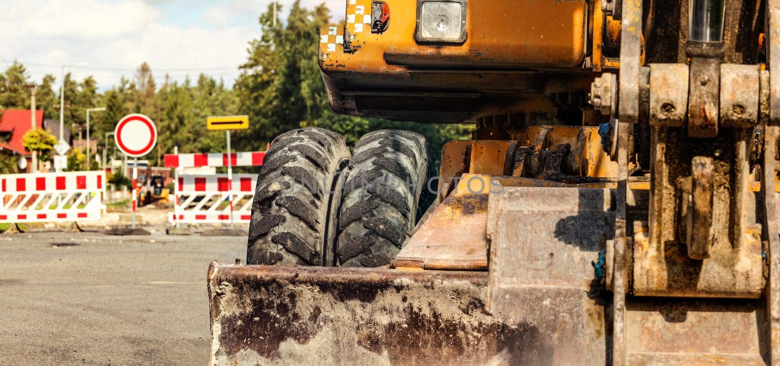 Detail on old yellow digger machine back, road closed signs, construction in progress background. Roadworks concept banner by Ivanko