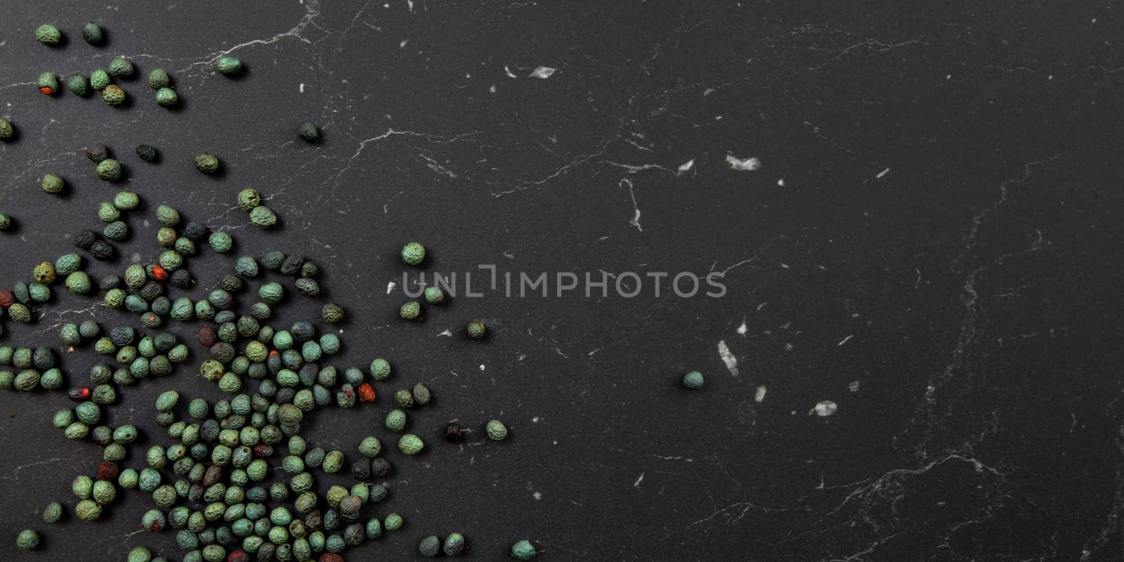 Tabletop view, Black pepper (Piper nigrum) spice spilled on dark marble like board. Turkish green / blue peppercorn variant. Banner with space for text on right.