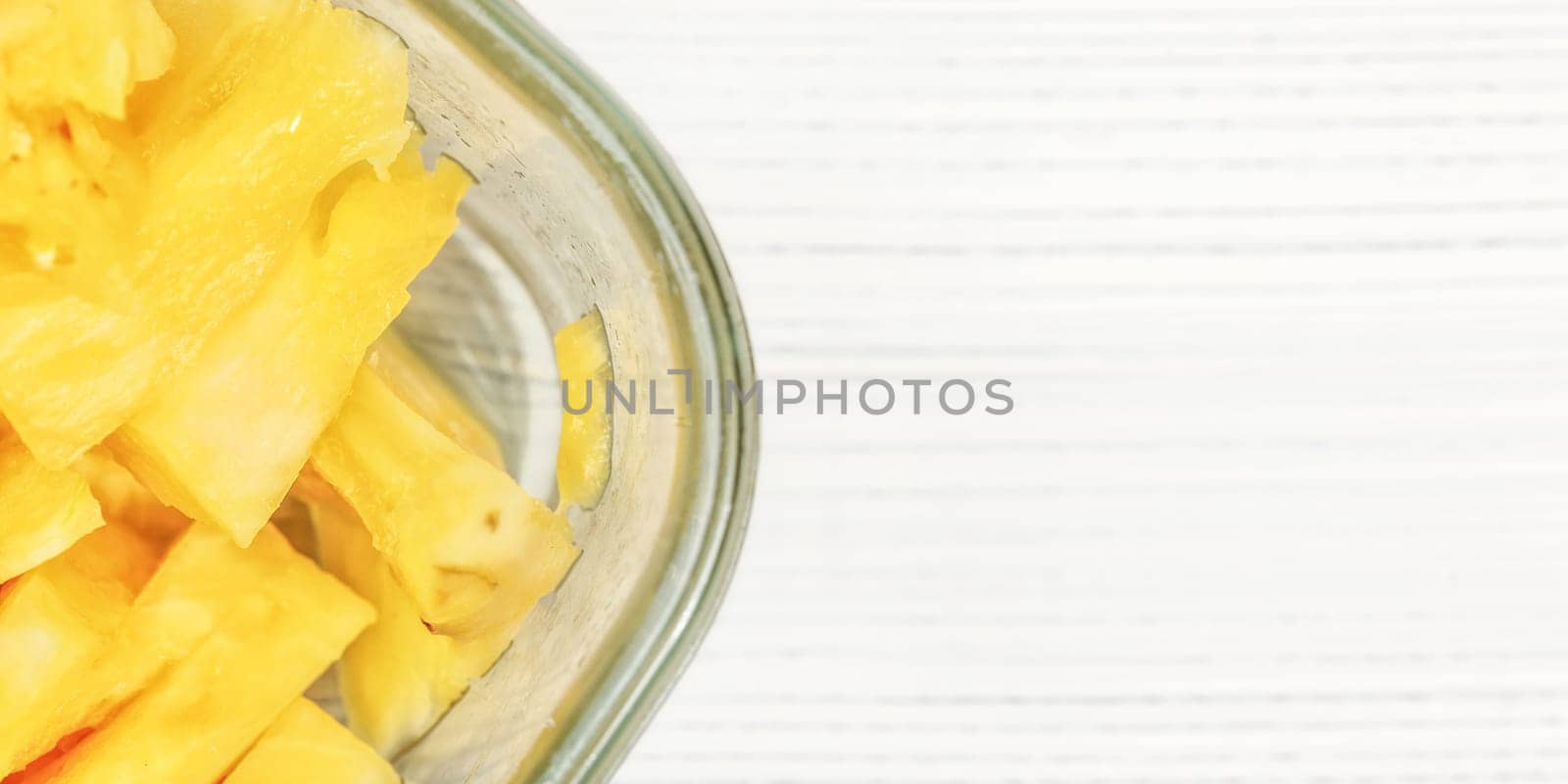 Tabletop view, detail - pieces of juicy pineapple in glass bowl on white boards desk.