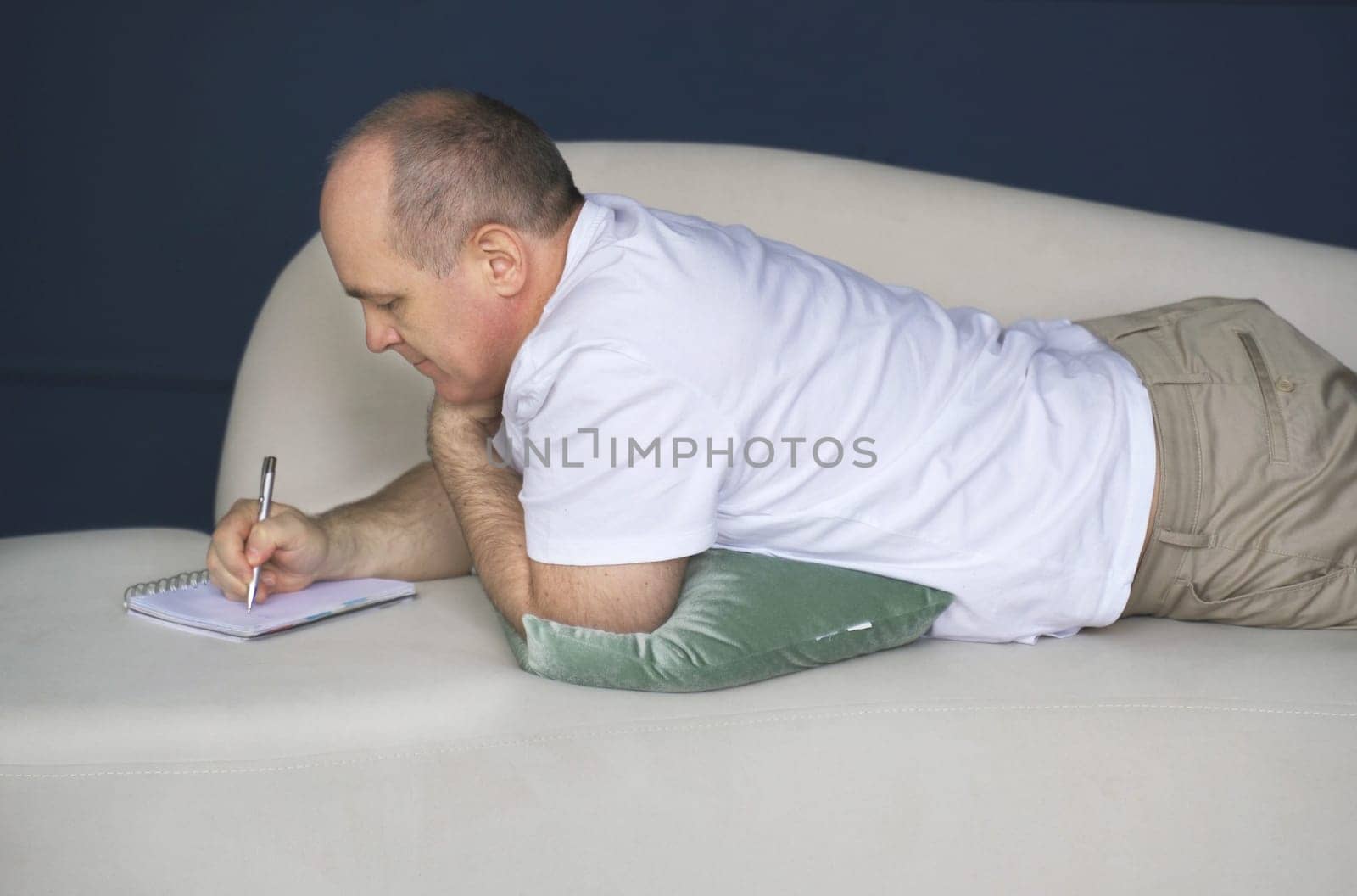 Young man lying on sofa and writing to do list in notepad