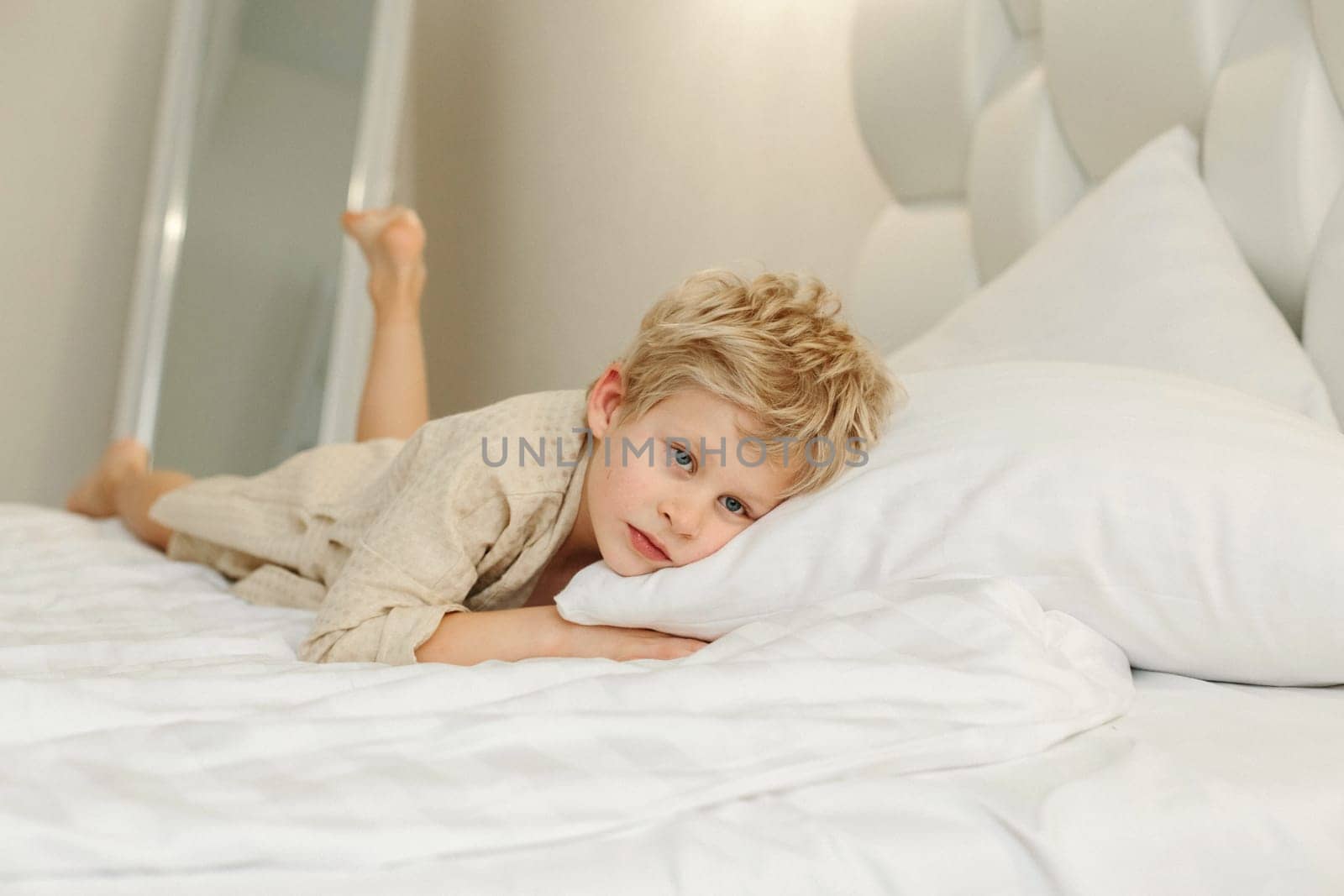 Portrait of a boy in a bathrobe, who lies on the bed and looks at the camera.