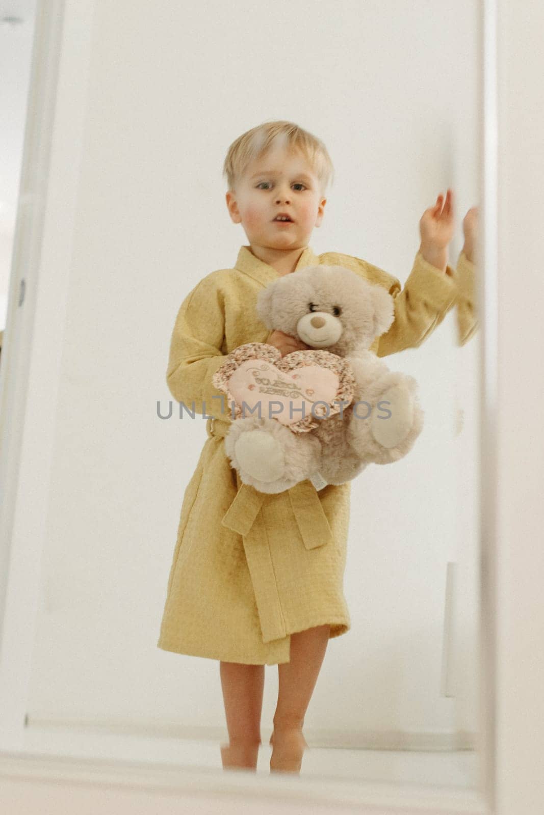 Portrait of a boy reflected in the mirror. A boy in a bathrobe hugs a bear soft toy.