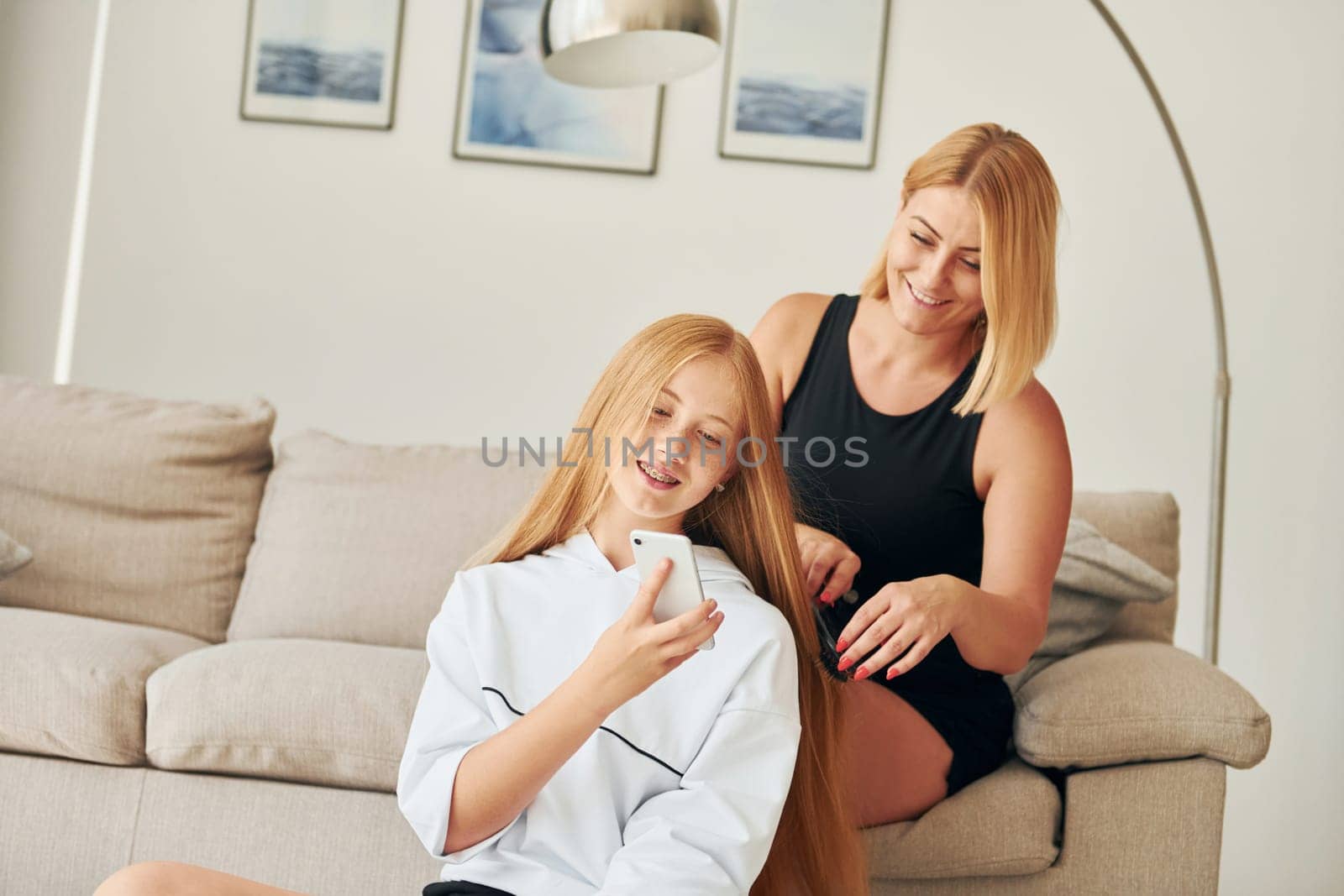Doing hairstyle. Female teenager with her mother is at home at daytime.