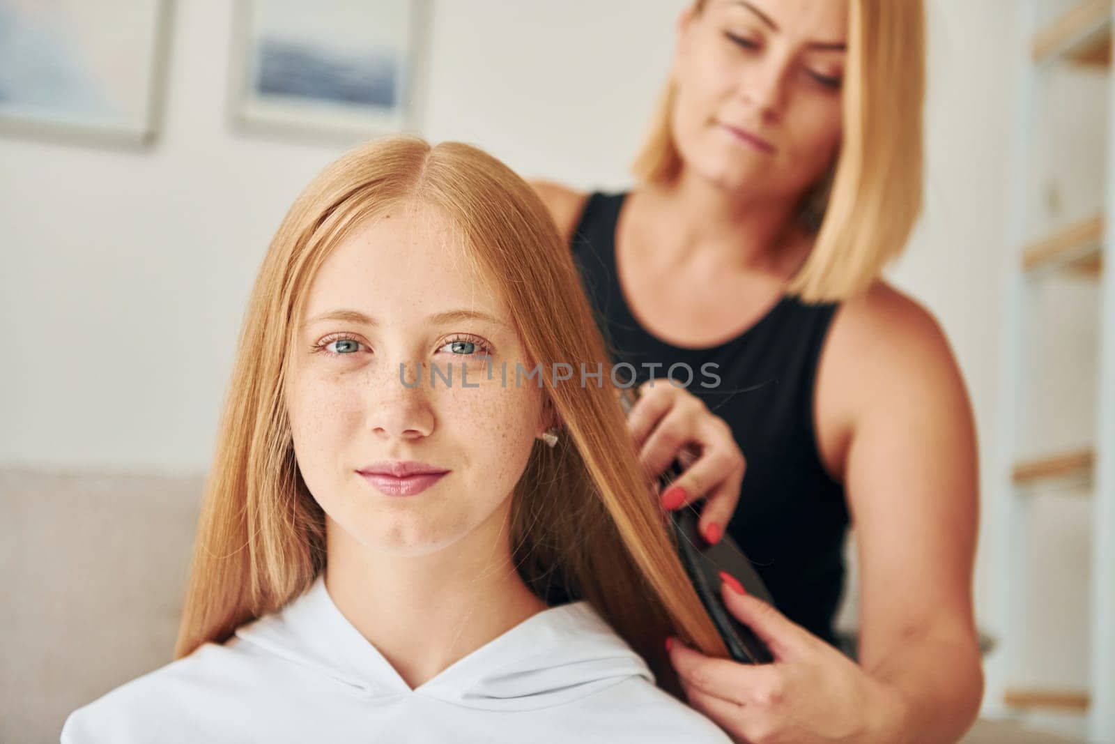 Doing hairstyle. Female teenager with her mother is at home at daytime by Standret