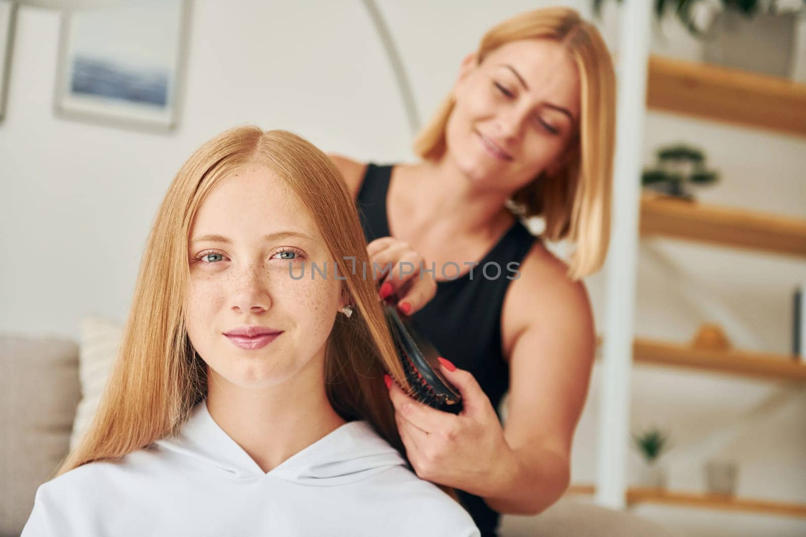Parent helping with hair. Female teenager with her mother is at home at daytime by Standret