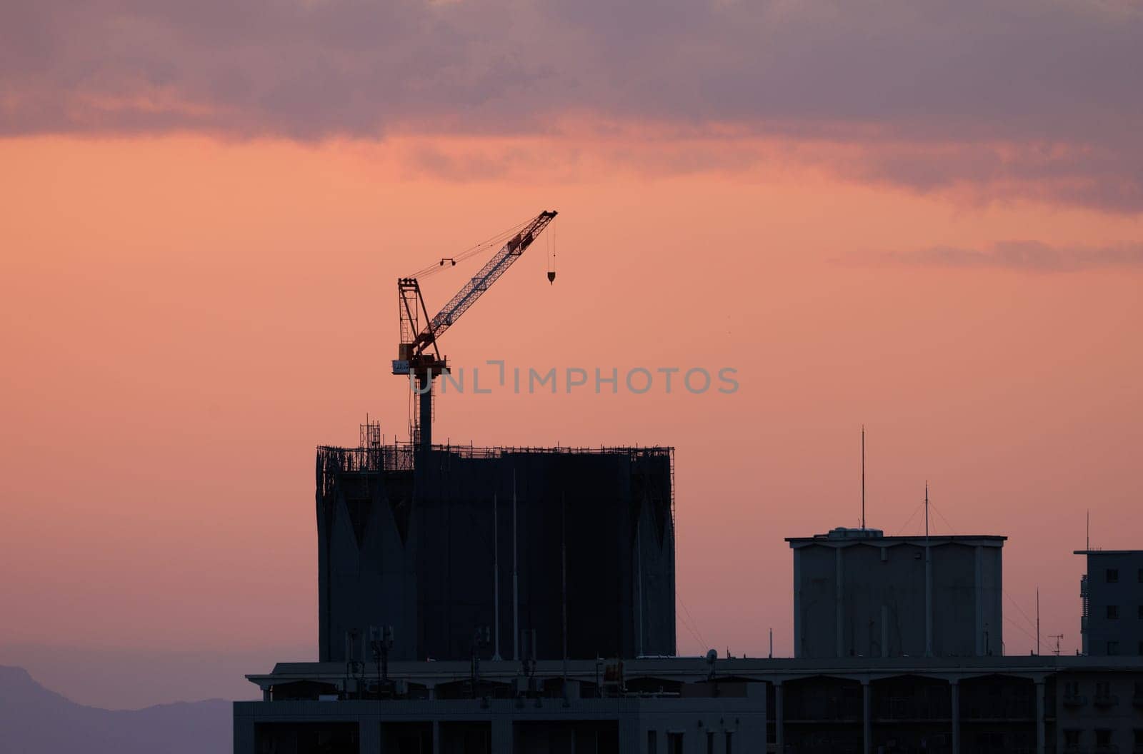 Rooftop crane atop low rise building after sunset by Osaze