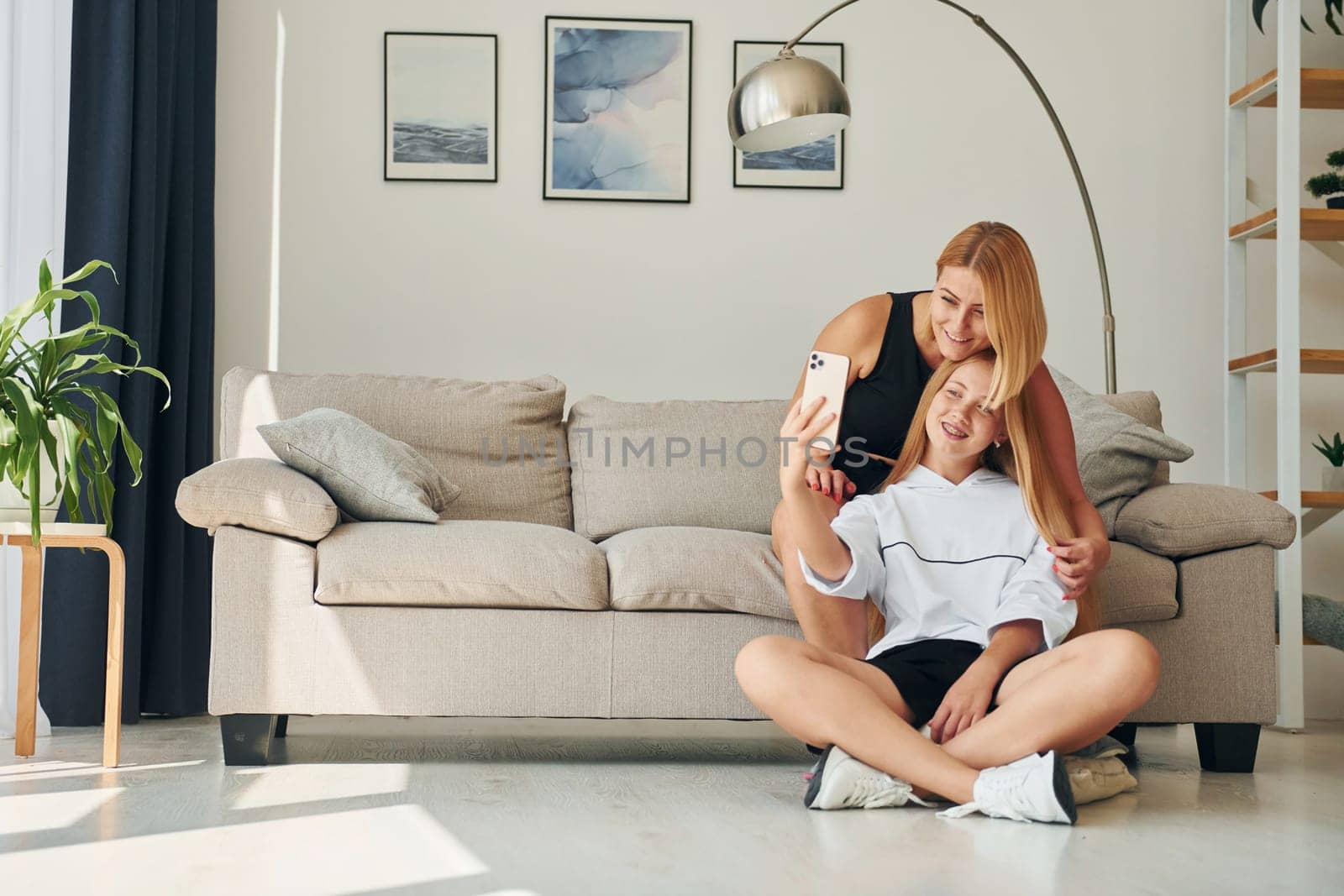 With phone in hands on the floor. Female teenager with her mother is at home at daytime by Standret