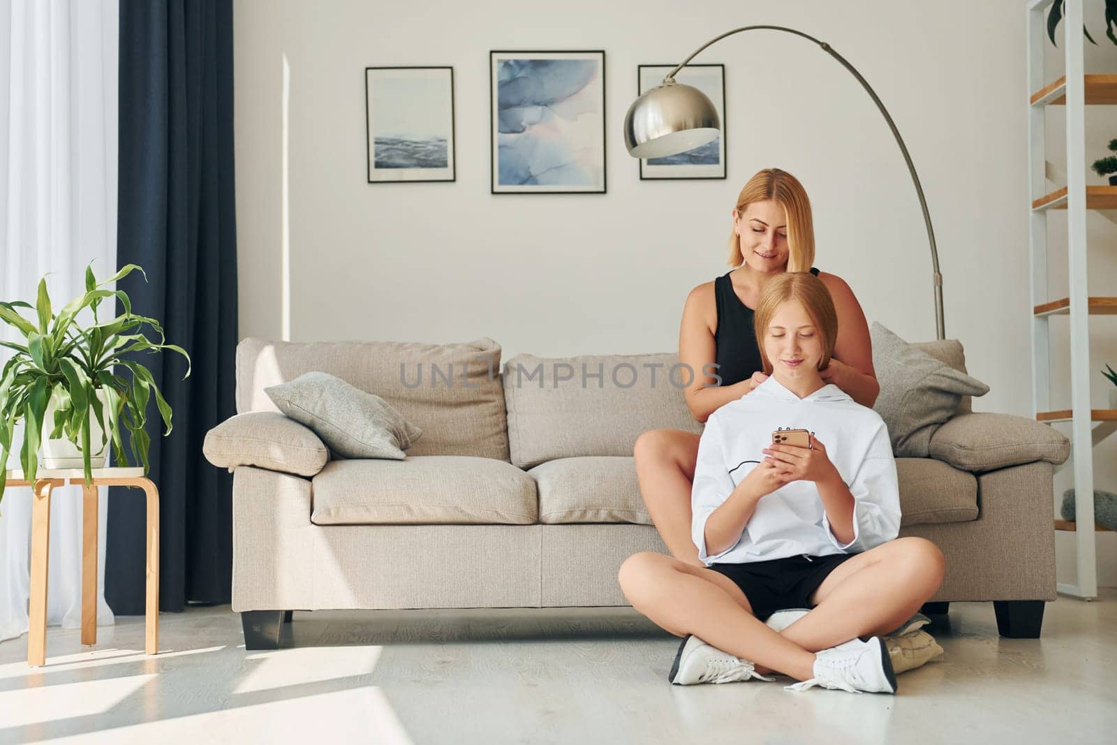 With phone in hands on the floor. Female teenager with her mother is at home at daytime by Standret