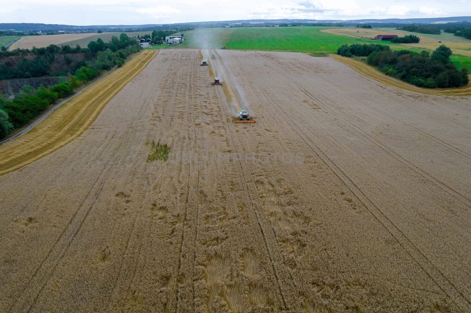 Three combine harvesters in the field harvest wheat, harvesting wheat grain, high yield. Work of harvesters in the field. Top view of the field and harvesters.