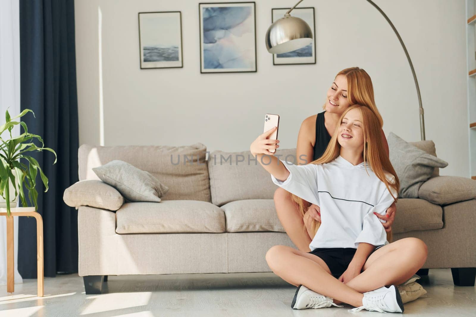 Sitting on the floor. Female teenager with her mother is at home at daytime by Standret