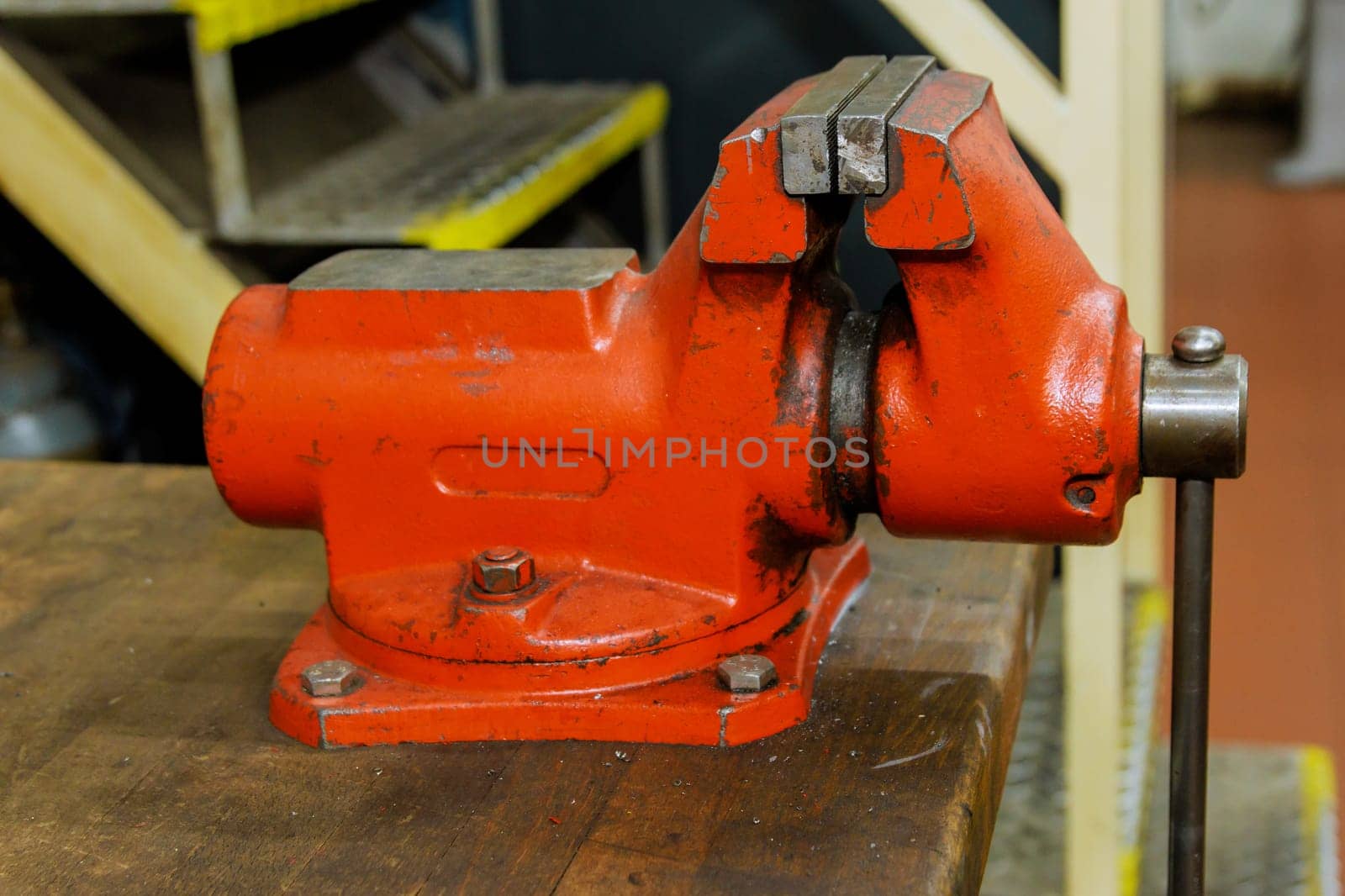 The vise is fixed on the metalworking workbench. A red vise on a wooden workbench at a metalworking plant. Bench tools.