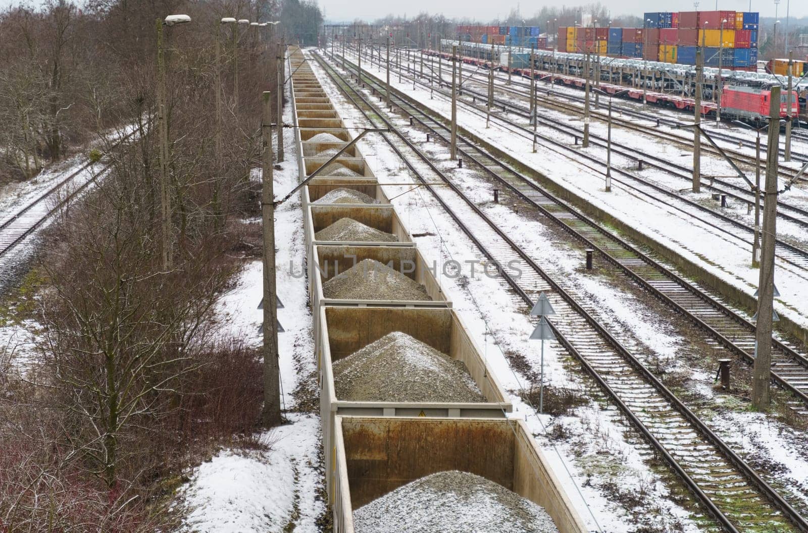 Railway wagons with gravel parked on sidings. In the background, containers and wagons loaded with cars are out of focus.