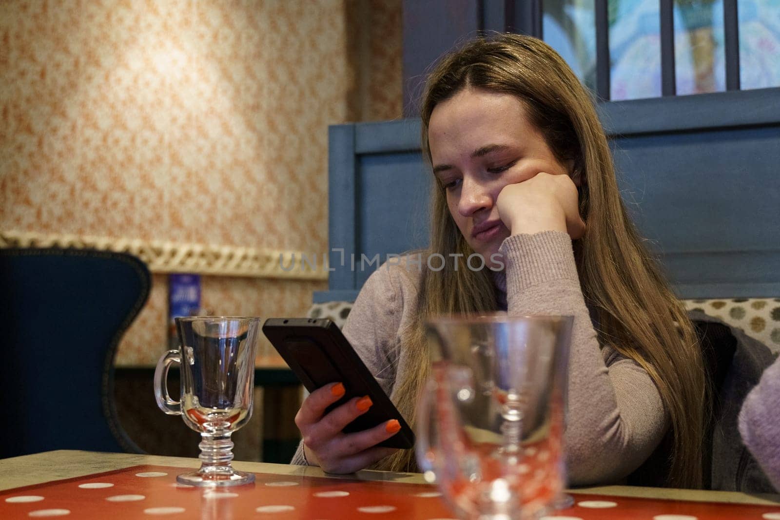 A young woman is sitting in a cafe, looking into a smartphone, waiting. Close-up.