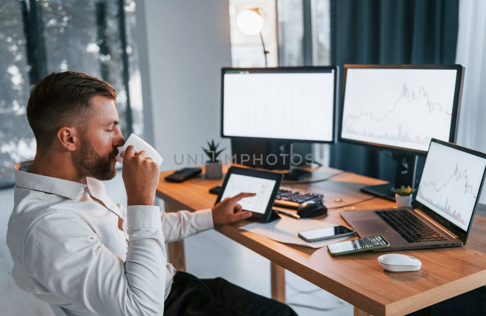Busy day. Young businessman in formal clothes is in office with multiple screens.