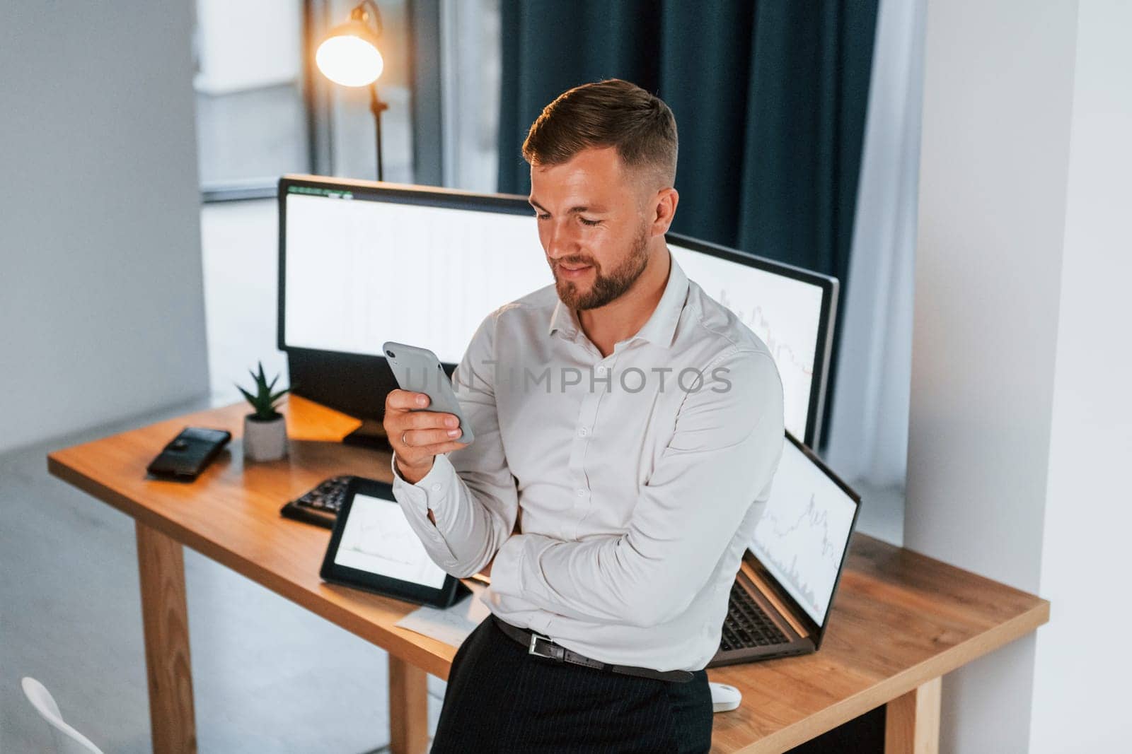 Busy day. Young businessman in formal clothes is in office with multiple screens.